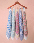 Five patterned cotton hand block printed bandana in blue, white, pink, and purple hanging from a wooden hanger against a soft pink background.