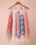 Five patterned cotton Hand block printed bandana in red, white, pink, blue, and peach hang from a wooden hanger with clothespins against a soft beige background.